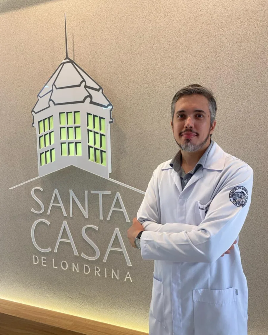 Dr. Marcelo Simplício Carvalho de jaleco, diante do letreiro da Santa Casa de Londrina